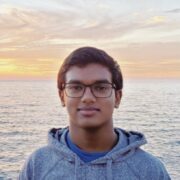 A portrait of Rohit De standing in front of the ocean