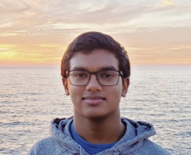 A portrait of Rohit De standing in front of the ocean